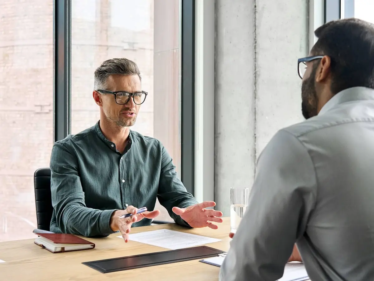 Two executives in a glass-walled office discussing a transaction